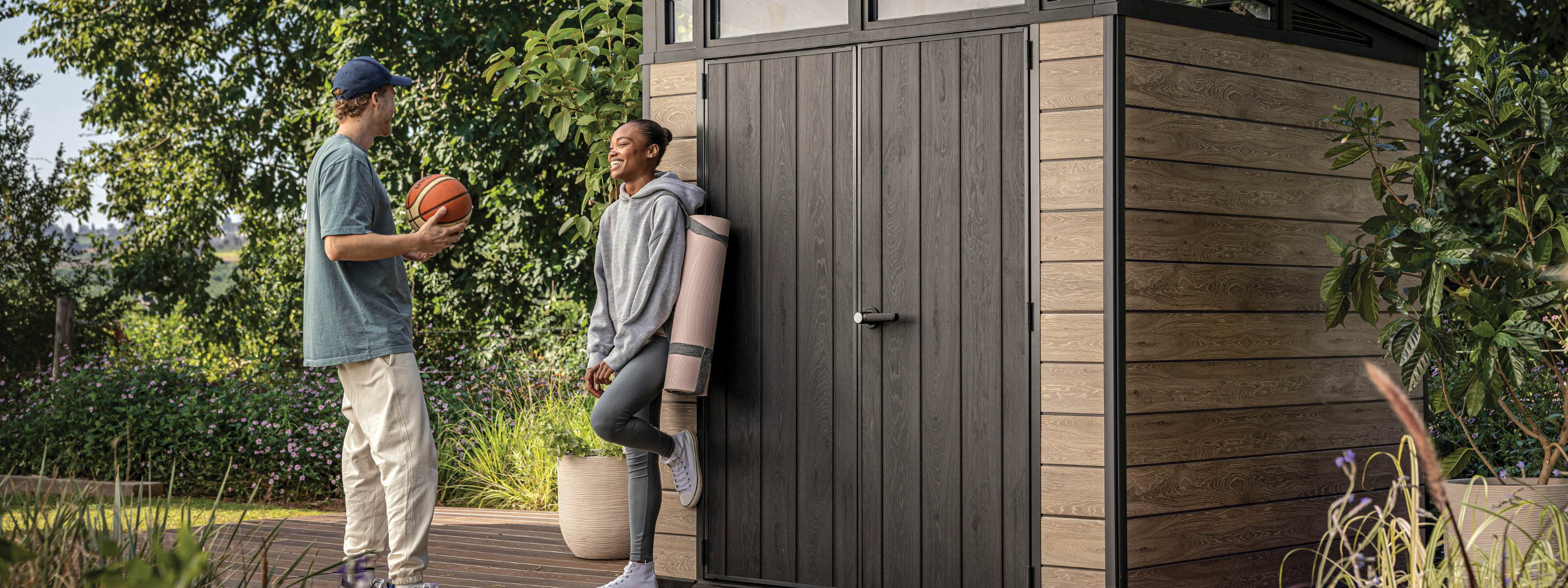 Outdoor toy storage shed in a garden with two people chatting beside a modern wooden unit.