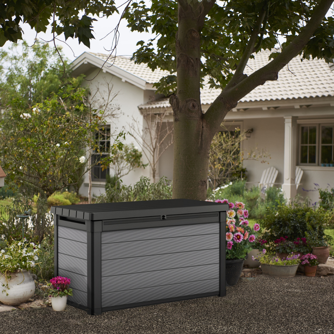 Premier 380L Storage Box in dark grey with a textured panelled exterior and hinged lid in a landscaped garden