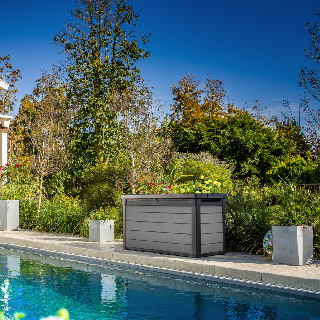 Premier 380L Storage Box in dark grey with a slatted lid beside a swimming pool and lush garden planting