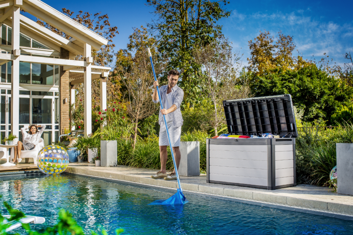 Denali 570L Storage Box in grey with its open lid beside a swimming pool while a person cleans the water