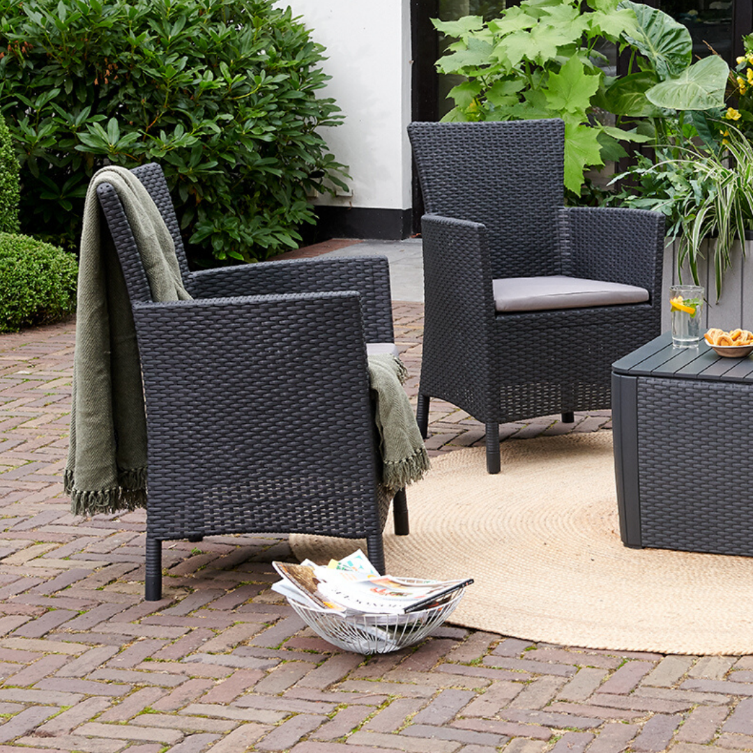 Iowa Balcony Set with two dark flat-wicker armchairs and cushions beside a matching storage side table in a garden setting