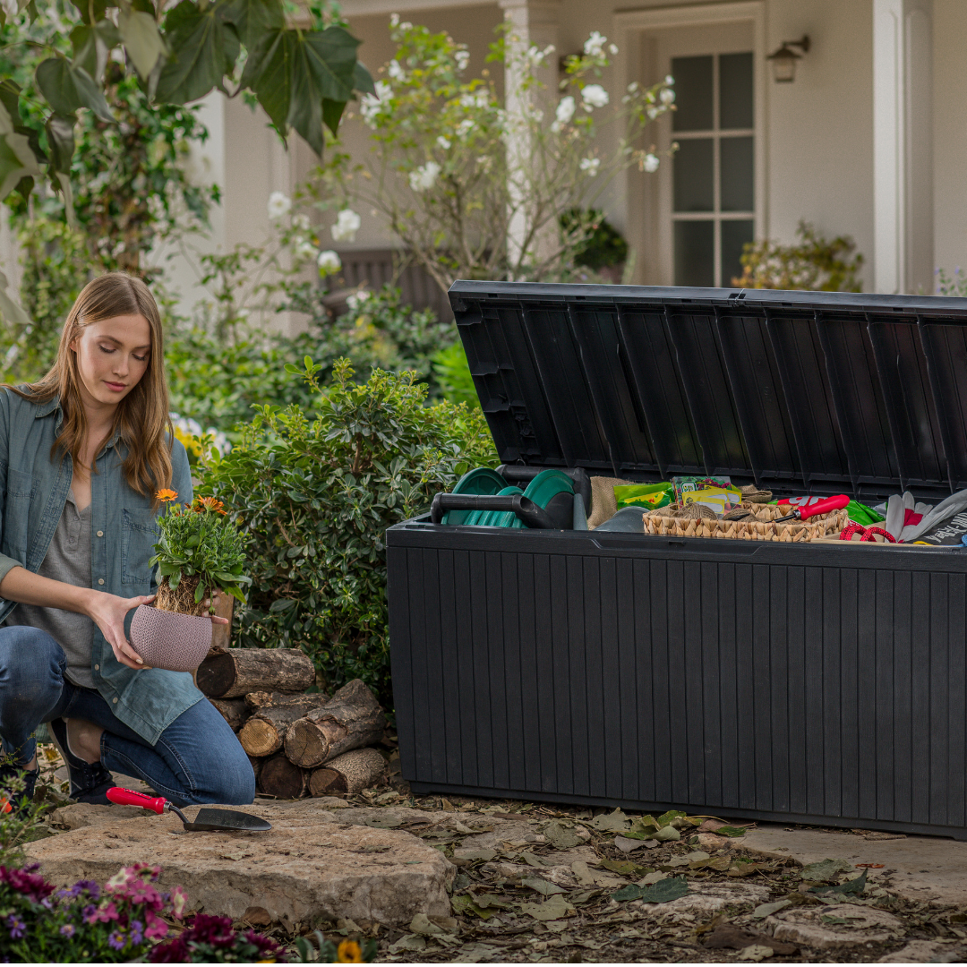 Springwood 305L Storage Box with open lid holding gardening tools and supplies while a gardener plants flowers nearby