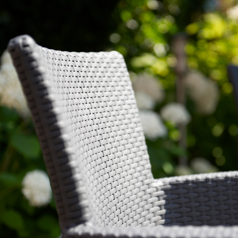 Iowa Balcony Set close-up of a light grey flat-wicker armchair with a curved back and armrest in a garden setting