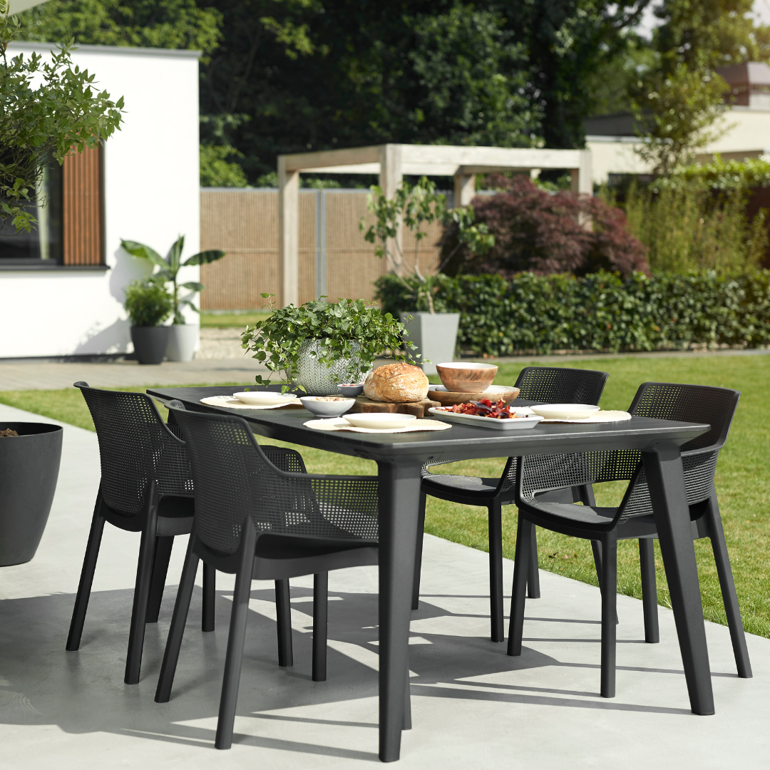 Lima Table - Graphite with a wood-look textured surface surrounded by black dining chairs in a sunny patio setting
