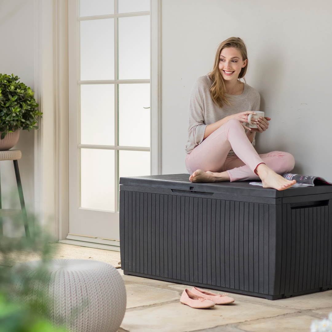 Springwood 305L Storage Box in dark grey with ribbed panels and a closed lid supporting a seated woman indoors