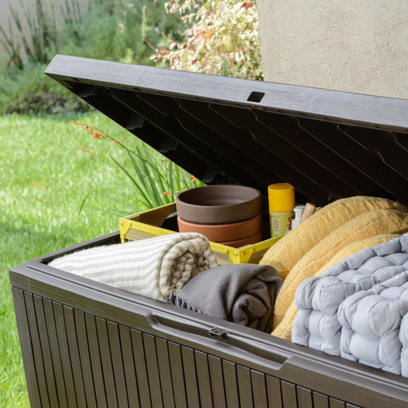 Springwood 305L Storage Box with open hinged lid revealing folded blankets cushions plant pots and garden supplies in a woodgrain finish