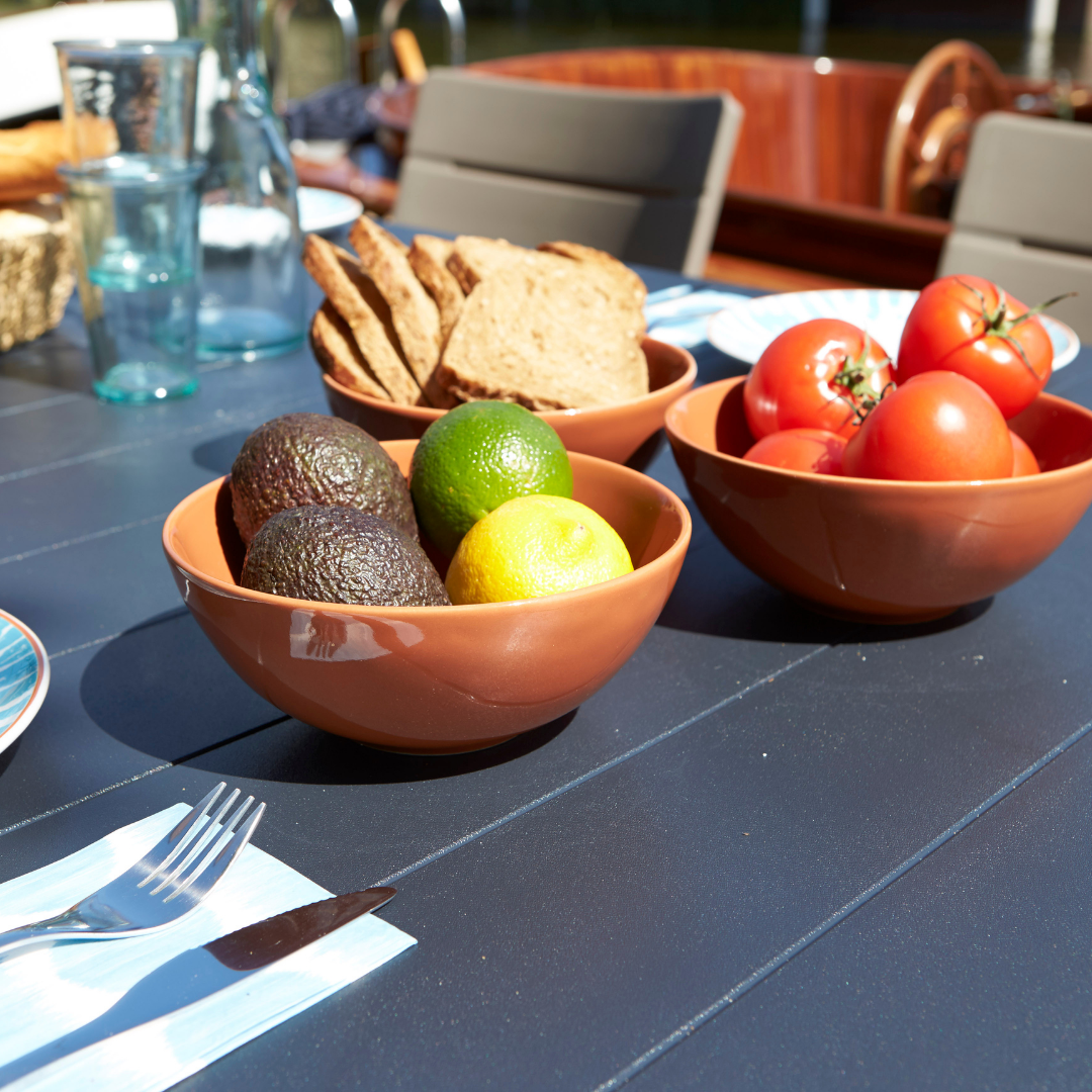 Lima Table in graphite with a wood-look tabletop set for outdoor dining with bowls of fruit bread and tableware