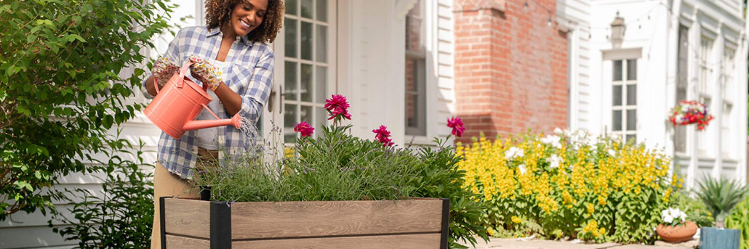 Woman watering flowers in a Keter raised garden bed during a spring outdoor refresh in South Africa.