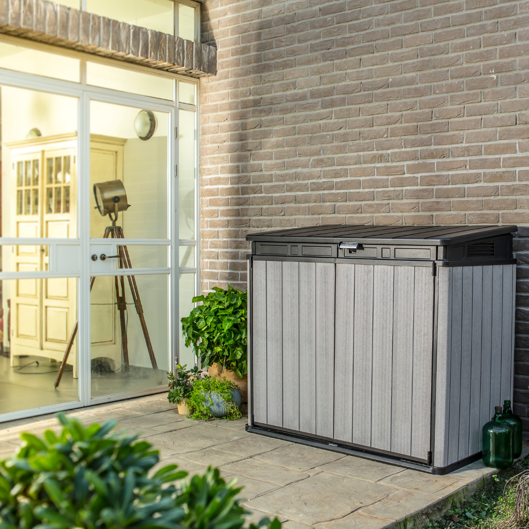 Elite Store outdoor storage unit in grey ribbed resin with a black fitted lid beside a brick wall and glazed garden entrance