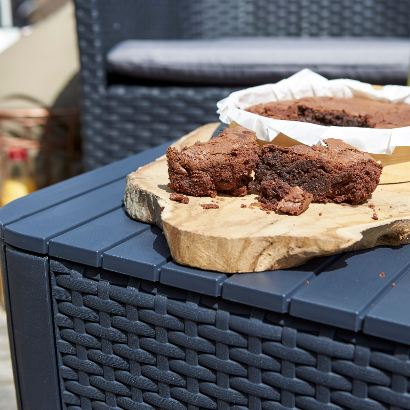 Iowa Balcony Set with a dark woven-effect side table topped by a wooden board and chocolate cake outdoors