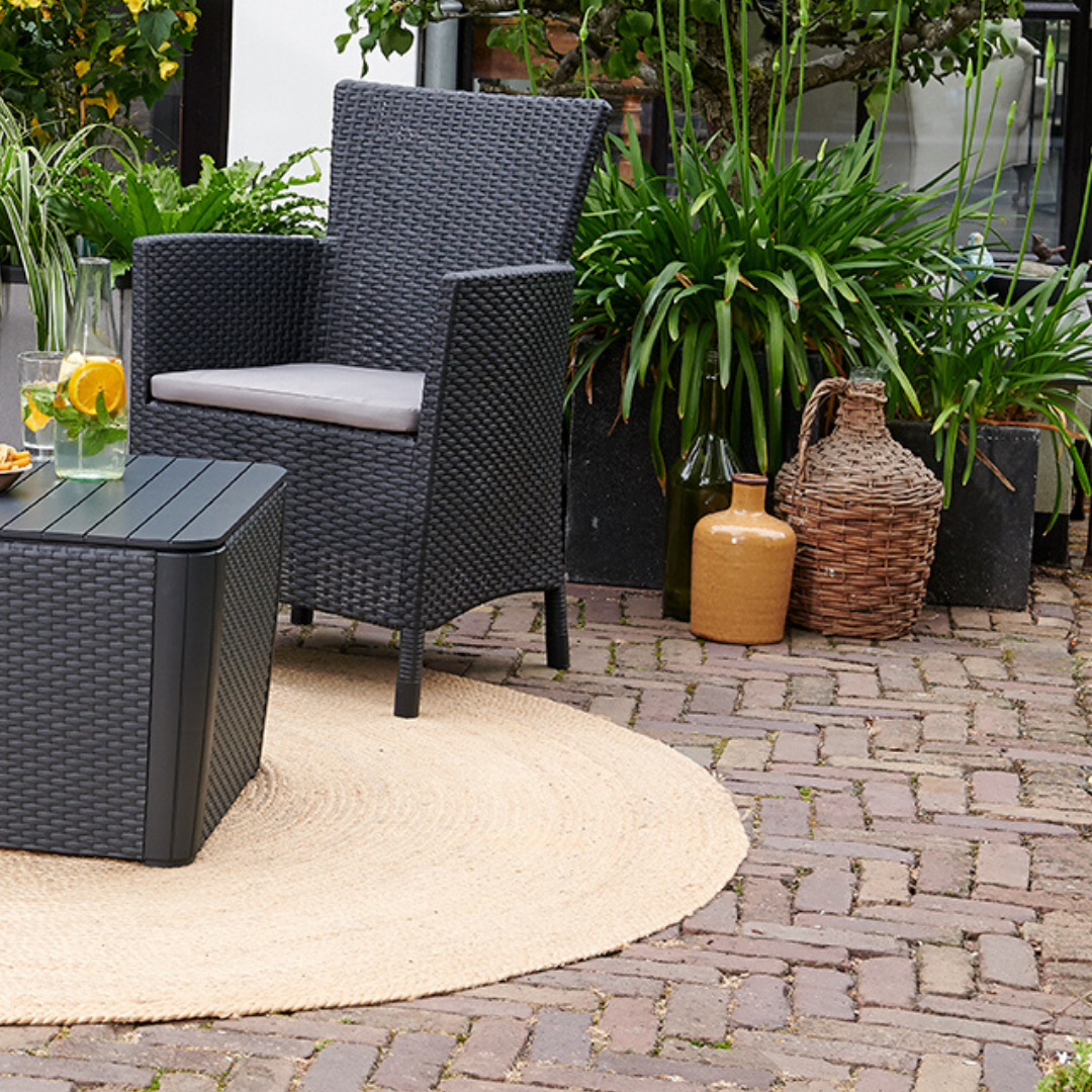 Iowa Balcony Set with a dark flat-wicker effect armchair and cushioned seat beside a matching storage side table on a paved patio